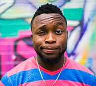 Portrait de Pierre, un homme souriant avec une chaîne et un t-shirt rose, identifié comme fêtard professionnel.